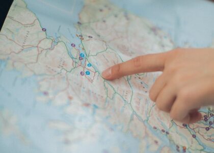 A woman's hand pointing at a location on a world map inside a car, highlighting navigation and travel planning.