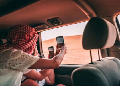 Tourists taking photos from inside a car in Dubai's desert landscape.